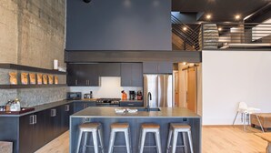 A modern kitchen with a central island, bar stools, and a staircase leading to an upper level. - Pet Friendly Loft / Rooftop Hot Tub & Views (Fernie)