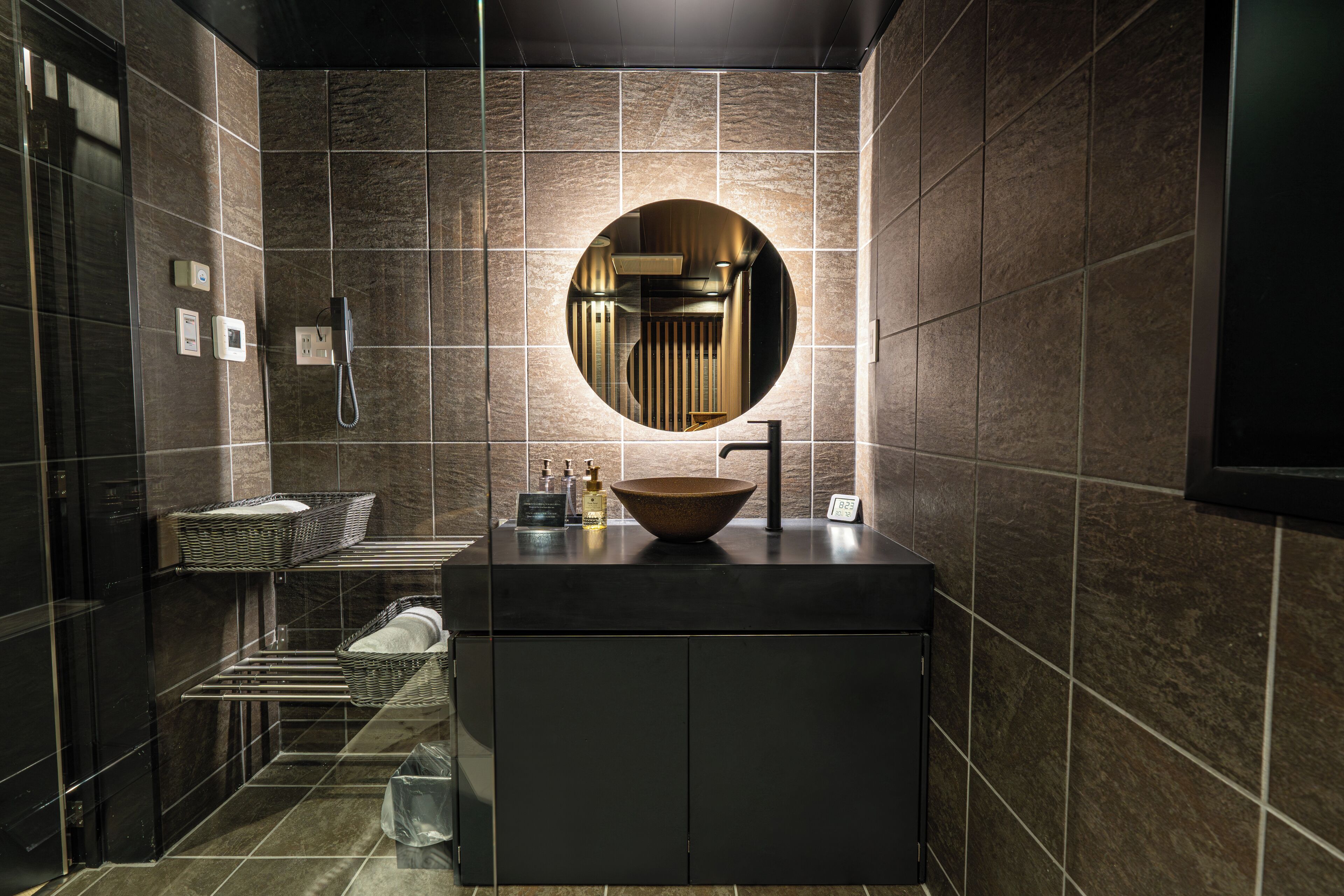 Een moderne badkamer met een grote ronde spiegel, een wastafel op standaard en een verwarmde handdoekhouder.