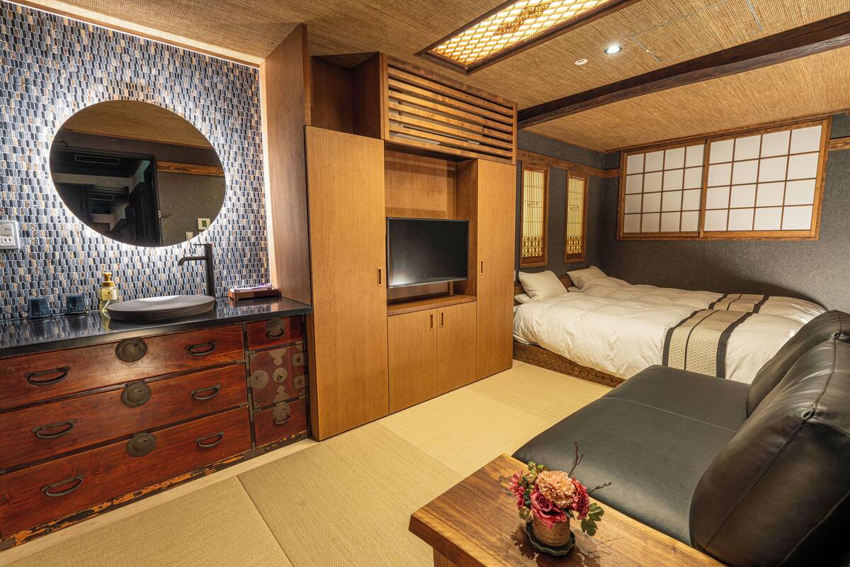A traditional Japanese-style room with tatami flooring, a wooden cabinet with drawers, a television, a bed with a futon, and a shoji screen.