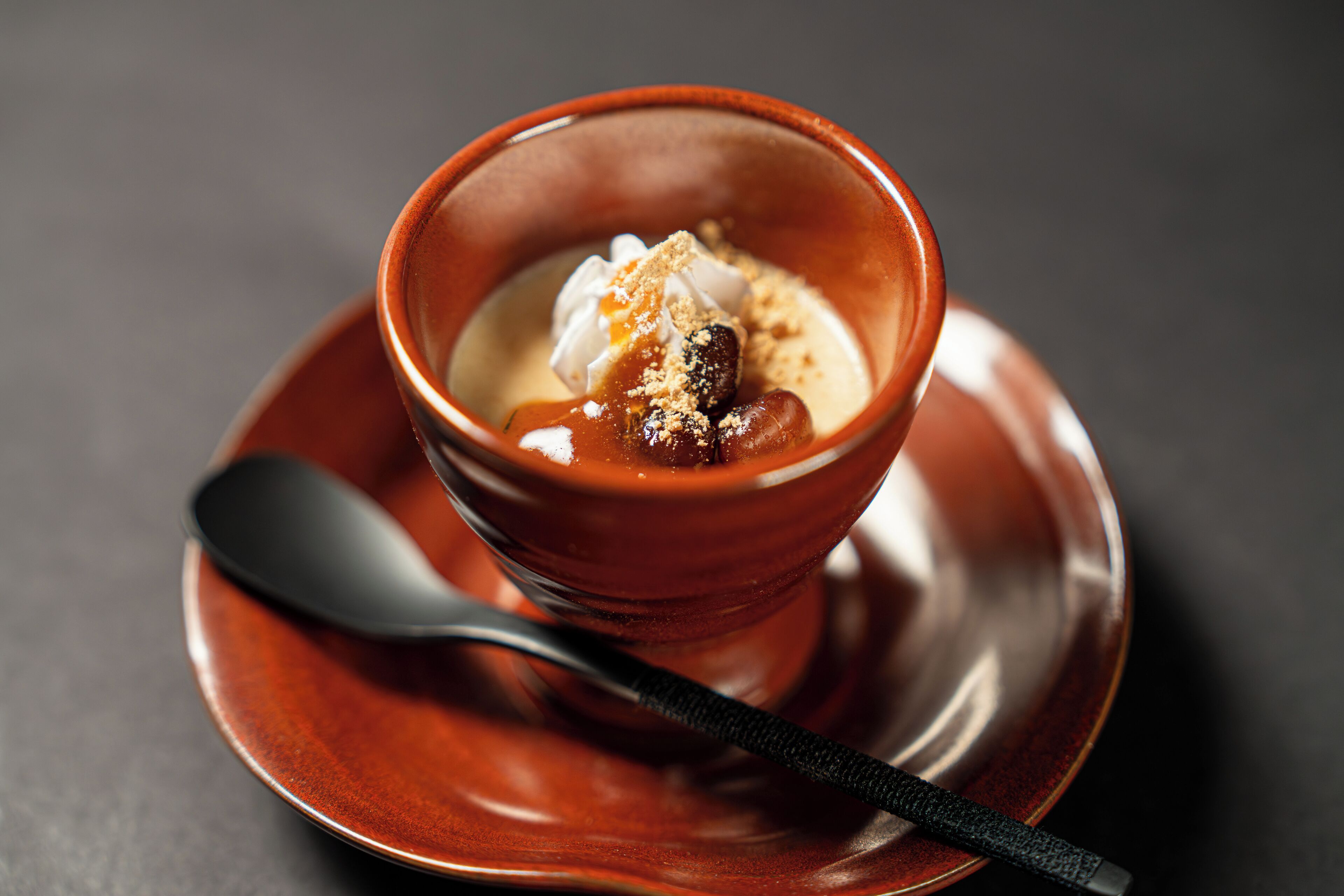 A dessert in a ceramic bowl on a saucer with a spoon.