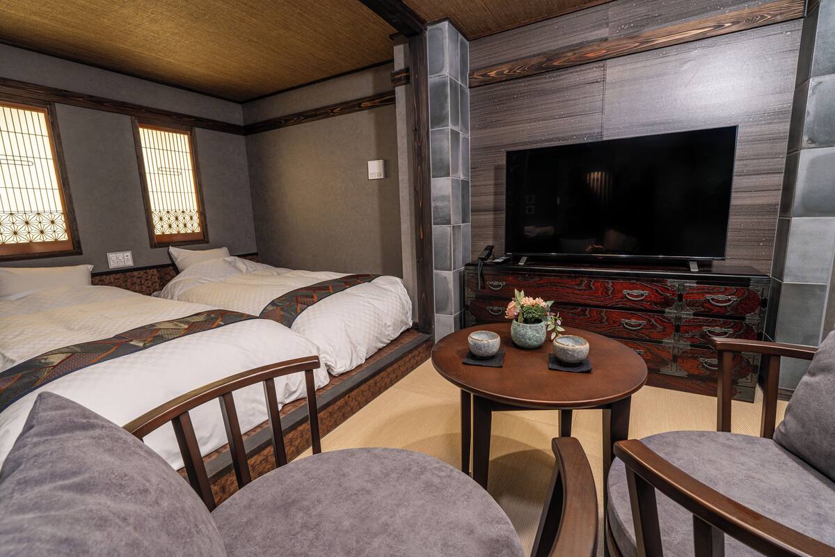 A hotel room with two beds, a TV, a wooden cabinet, and a small round table with chairs.