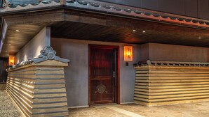 Une entrée de bâtiment de style traditionnel, avec une porte en bois, des marches en pierre et un toit recouvert de tuiles.