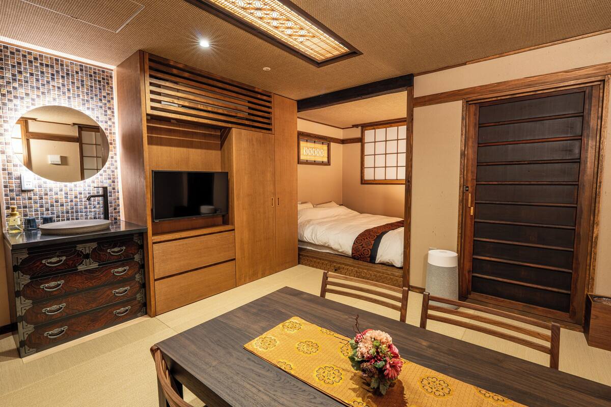 A traditional Japanese-style room with a tatami mat table, a wooden cabinet with drawers, a bed with a futon, and a sliding door.