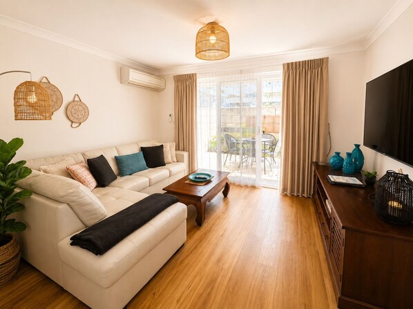 A living room with a sofa, coffee table, and a TV on a wooden cabinet. - Cape View 26 - Vila Cinta (Broadwater)