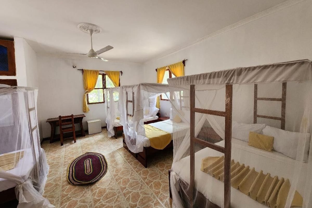 A room with two beds, a ceiling fan, and a window with curtains.