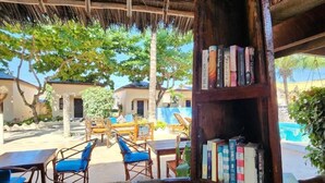 An outdoor seating area with wooden furniture and a bookshelf filled with books. - Seagull Nungwi Resort (Nungwi)