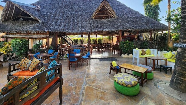 An outdoor seating area with thatched-roof structures, wooden furniture, and tropical plants. - Seagull Nungwi Resort (Nungwi)