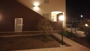 Un bâtiment moderne avec un escalier menant à une porte, un petit jardin et une voiture garée.