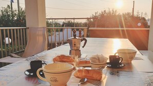 Un coin petit-déjeuner installé sur un balcon, avec une table, une machine à café, des tasses et des viennoiseries.