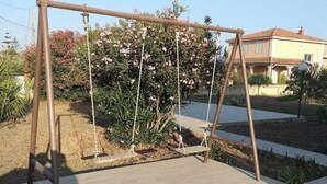 Une balançoire dans un jardin, avec une maison en arrière-plan.