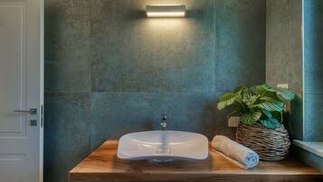 Un bagno con un mobiletto contenitore in legno, un lavandino bianco, una pianta in vaso e un asciugamano.