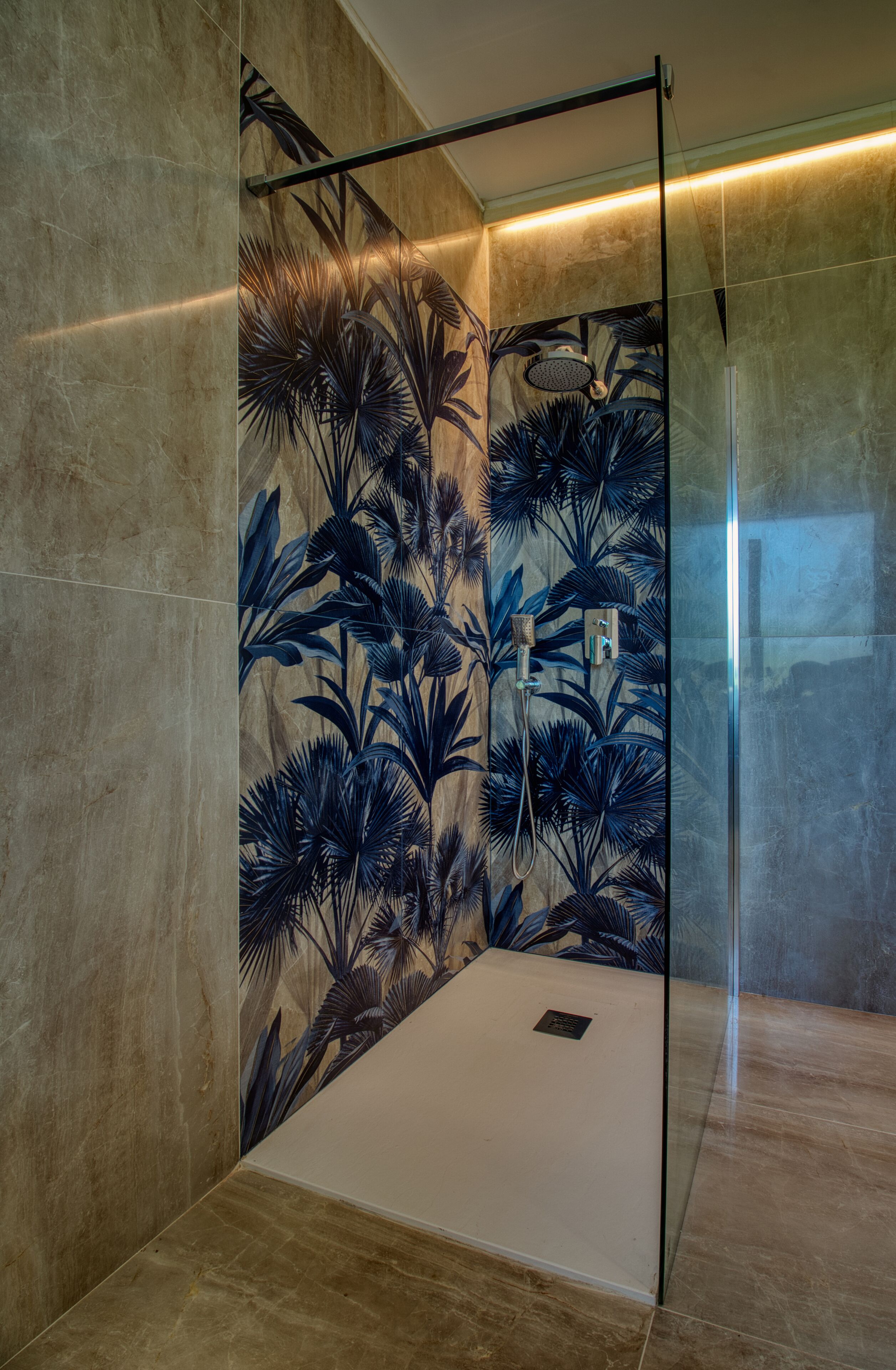 A modern shower with a glass door, a wall with a tropical leaf pattern, and a marble floor.