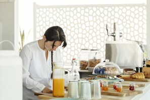 A breakfast setup with a glass of orange juice, jars of jam, and a bread display. - Posada El Convento Superior Deluxe Studio (Ayamonte)