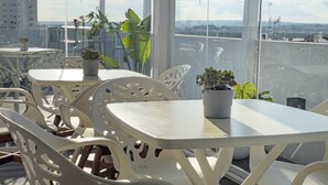 A rooftop terrace with white plastic chairs and tables, potted plants, and a view of distant buildings and mountains. - Posada El Convento Superior Deluxe Studio (Ayamonte)