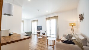 A modern hotel room with a wooden floor, a sofa, a dining table, and a TV. - Posada El Convento Superior Deluxe Studio (Ayamonte)