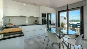 Une cuisine moderne avec des meubles blancs, une table à manger en verre et une vue sur l’extérieur.