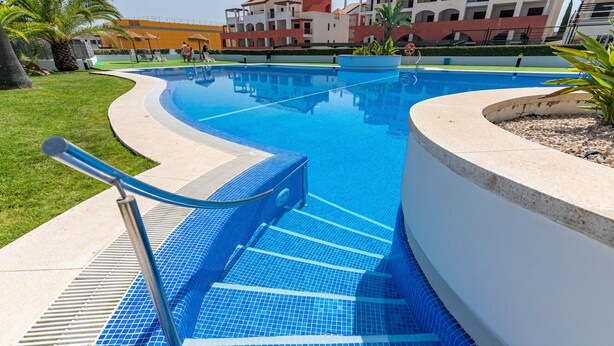 Une piscine avec une terrasse carrelée de bleu, un poste de surveillance pour les sauveteurs et un palmier en arrière-plan.