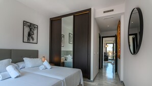 Une chambre d’hôtel avec un grand lit, une armoire, un miroir et un couloir menant à un coin salon.