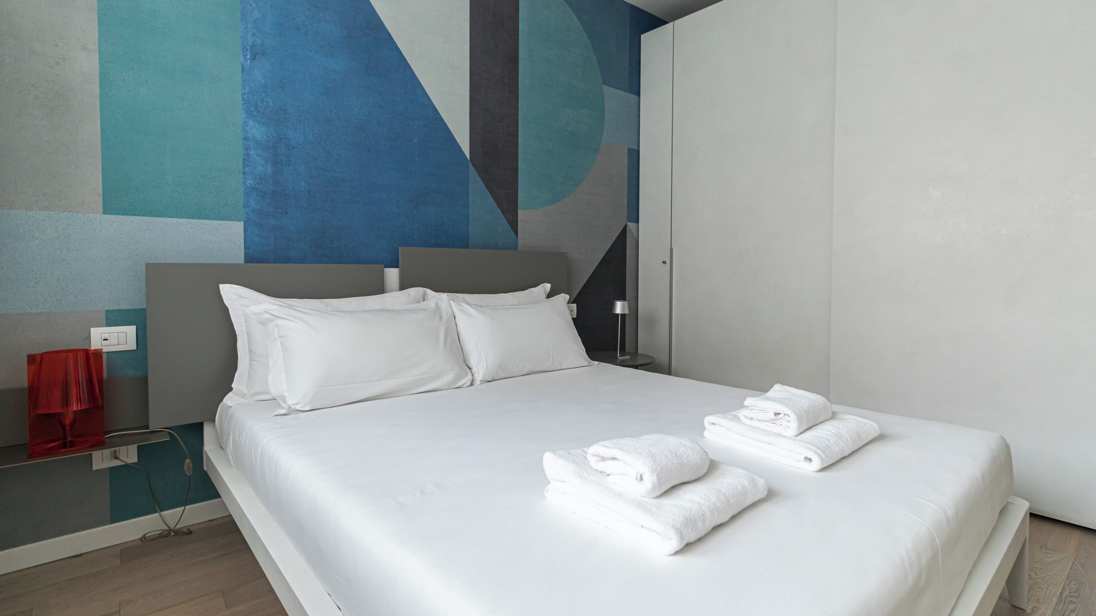 A modern hotel room with a large bed, white linens, and a geometric wall design.