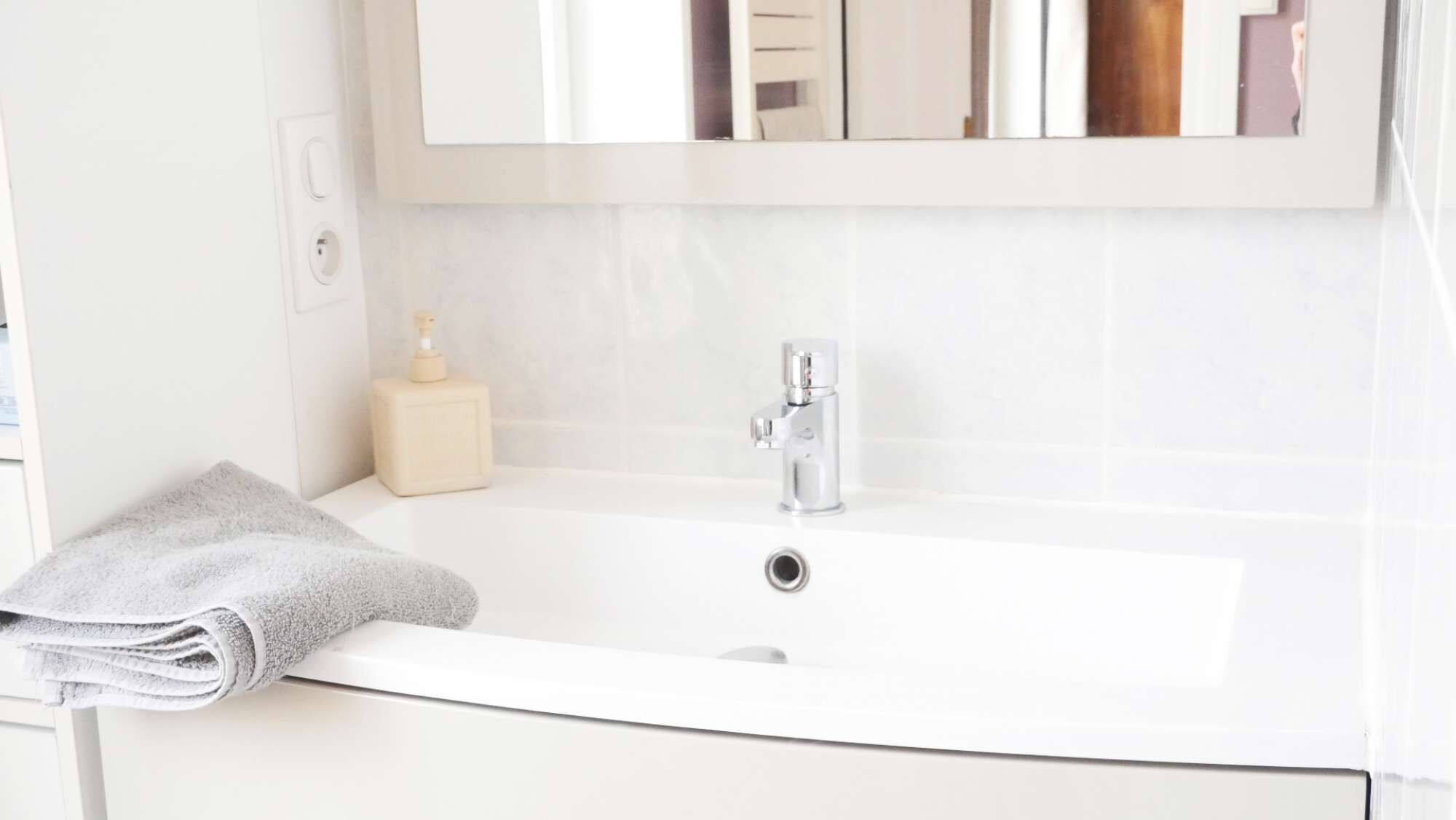 Een badkamer met een witte wastafel, een spiegel erboven en een handdoek ernaast.