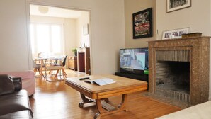 Un salon avec une table basse en bois, un téléviseur, une cheminée et, au fond, un coin repas.