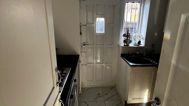 A narrow kitchen with a white door, a window with a view, and a tiled floor. - Cozy 2 Bedhouse 20mins From Manchester City Centre (Oldham)