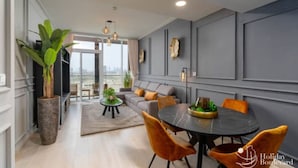Een moderne woonkamer met een grijze bank, een ronde eettafel met oranje stoelen, een grote potplant en een uitzicht op de stad.