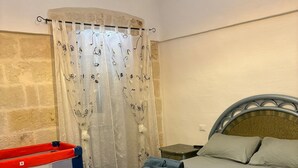 Een slaapkamer met een bed, een klein nachtkastje, een rode opbergunit en een gordijn met bloemenmotieven.