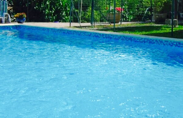 A swimming pool with clear blue water, surrounded by greenery and a fence.