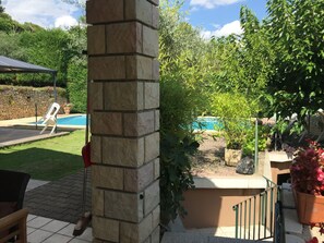 A stone pillar, a swimming pool, and a patio area with a chair and potted plants.