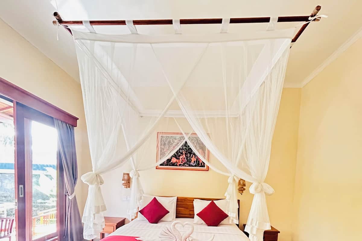 A bed with a canopy, a red bench, and a view of the outdoors.