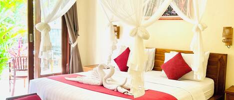 Una cama con dosel y cuatro columnas con un edredón rojo y blanco, un banco de madera y vistas al exterior con vegetación.