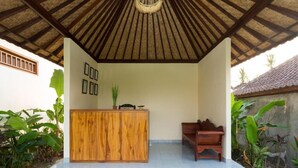 A reception area with a wooden desk, a bench, and a thatched roof. - Canting Bali Suite (Ubud)