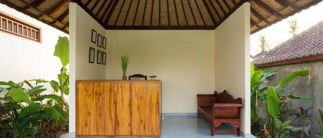 A reception area with a wooden desk, a bench, and a thatched roof.