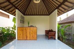 A reception area with a wooden desk, a bench, and a thatched roof. - Canting Bali Suite (Ubud)