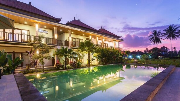 A large building with a swimming pool, surrounded by palm trees and a sunset sky. - Canting Bali Suite (Ubud)