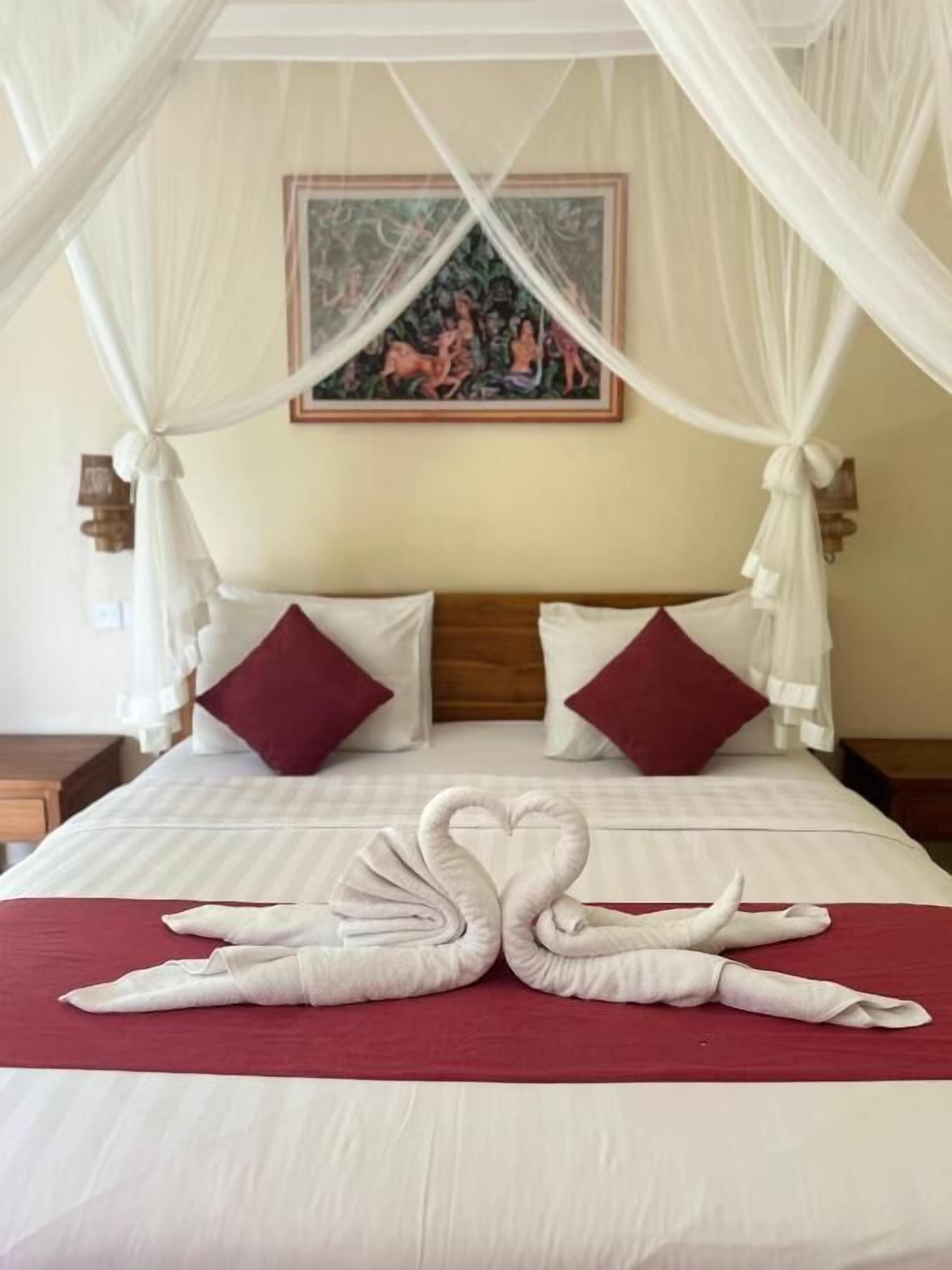 Ein Bett mit Baldachin, rote Kissen und einer Zyanus-Handtuch-Arrangement.