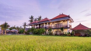 A two-story building with a red roof, surrounded by a green field, likely a hotel or resort. - Canting Bali Suite (Ubud)