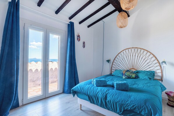 Een slaapkamer met een groot bed, uitzicht door een schuifdeur en een plafond met zichtbare balken.