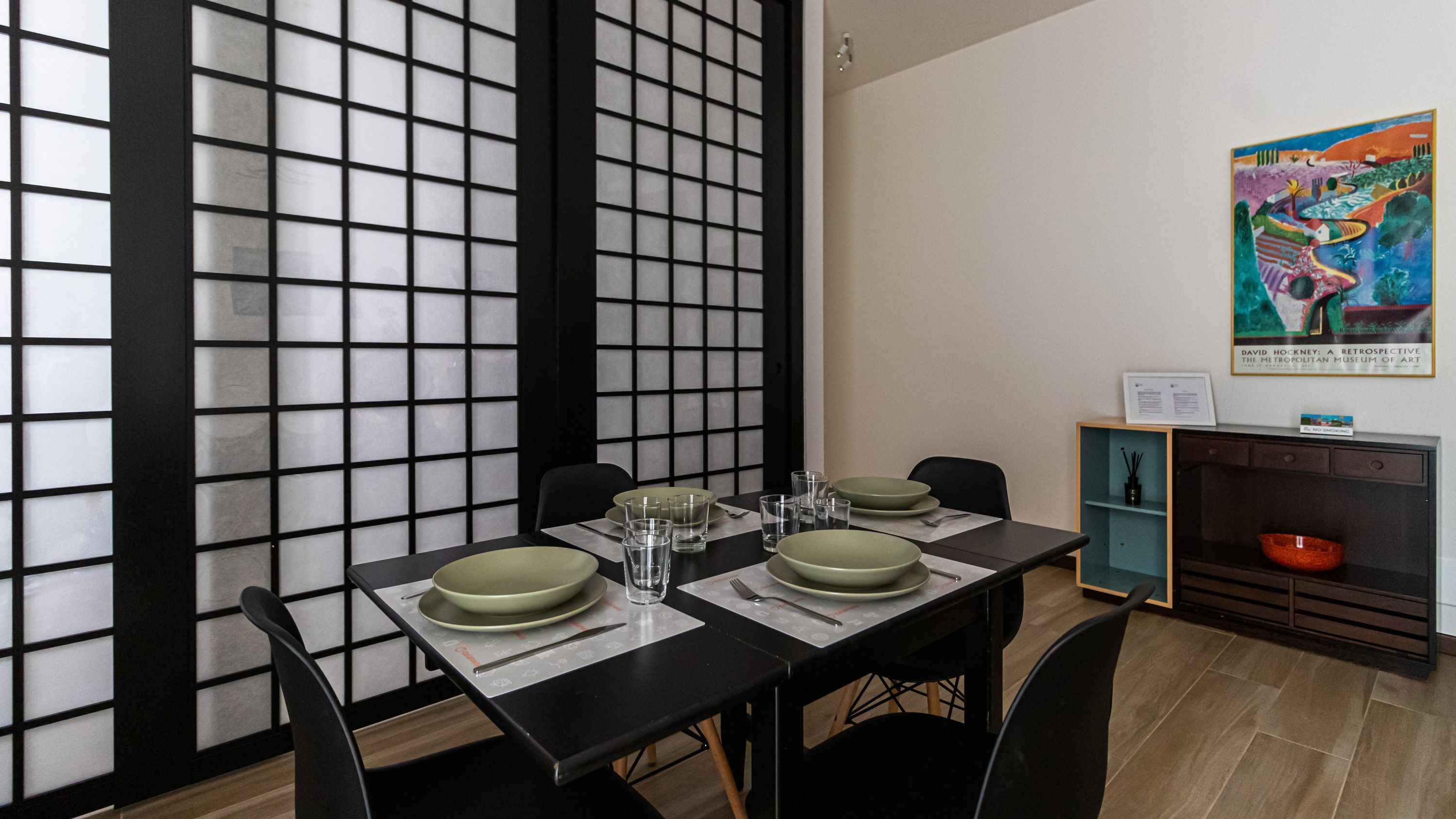 Een eetruimte met een tafel voor vier personen, stoelen, een decoratieve wand en een schilderij.