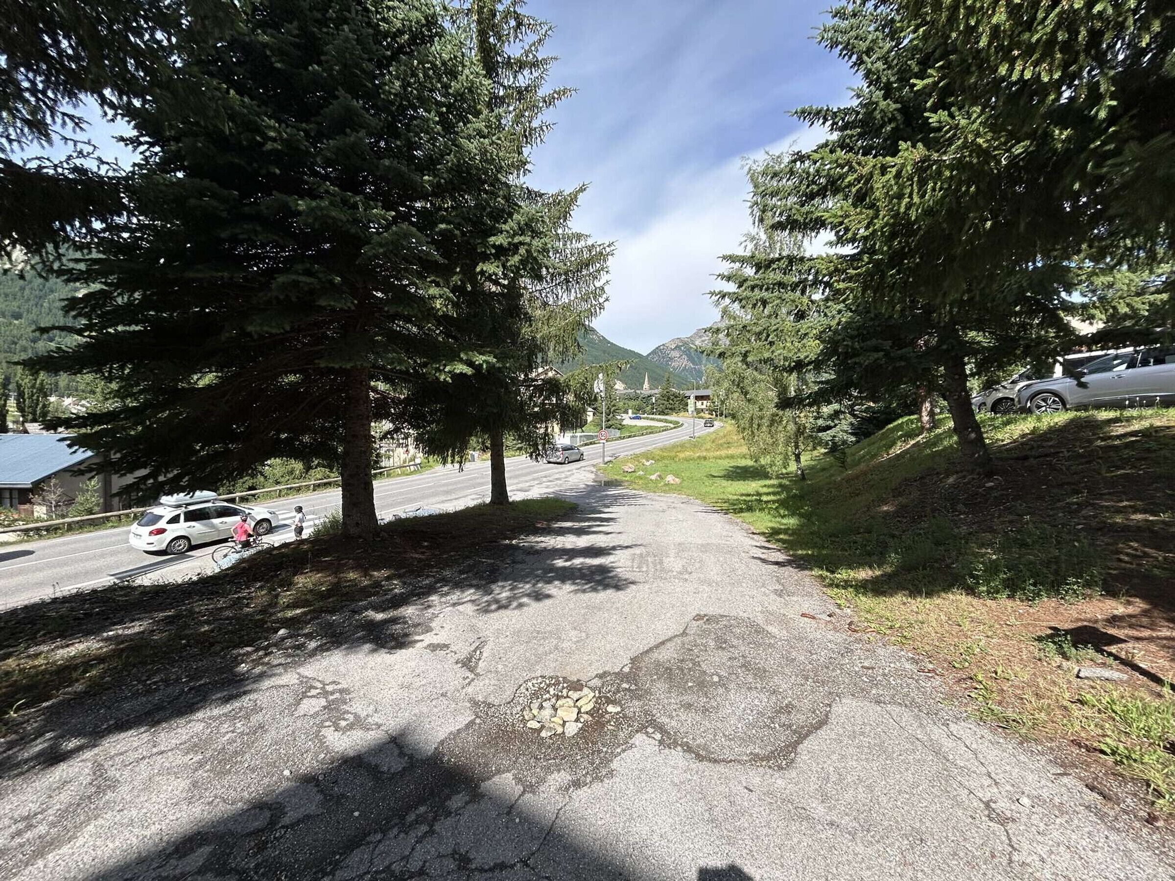 Un sendero pavimentado flanqueado por árboles que conduce a una carretera con vehículos.