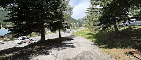 Un sendero pavimentado flanqueado por árboles que conduce a una carretera con vehículos.