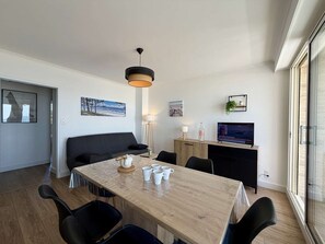 Uma sala de estar moderna com uma mesa de jantar de madeira, cadeiras pretas, sofá, televisão e obras de arte nas paredes.
