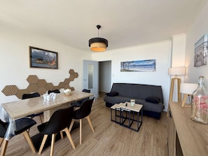 Uma sala de estar moderna com área de jantar, apresentando um sofá, uma mesa de centro, uma mesa de jantar com cadeiras e uma luminária pendente.