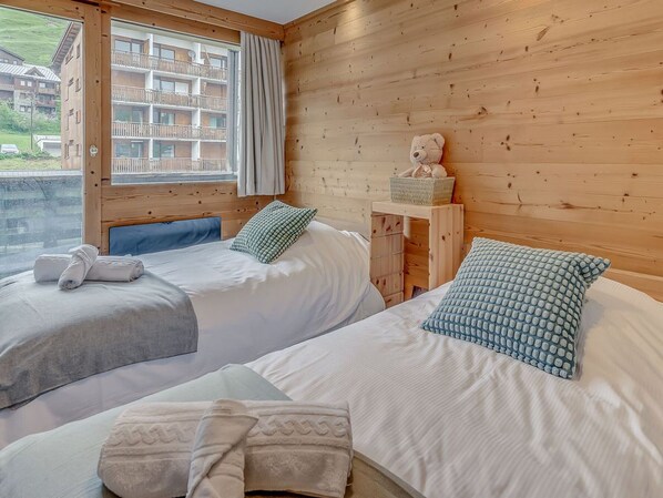 A room with two beds, a wooden headboard, a window with a view of a building, and a teddy bear on a nightstand. - Tignes - 3-room apartment, 6 pers, hotel services (Tignes)