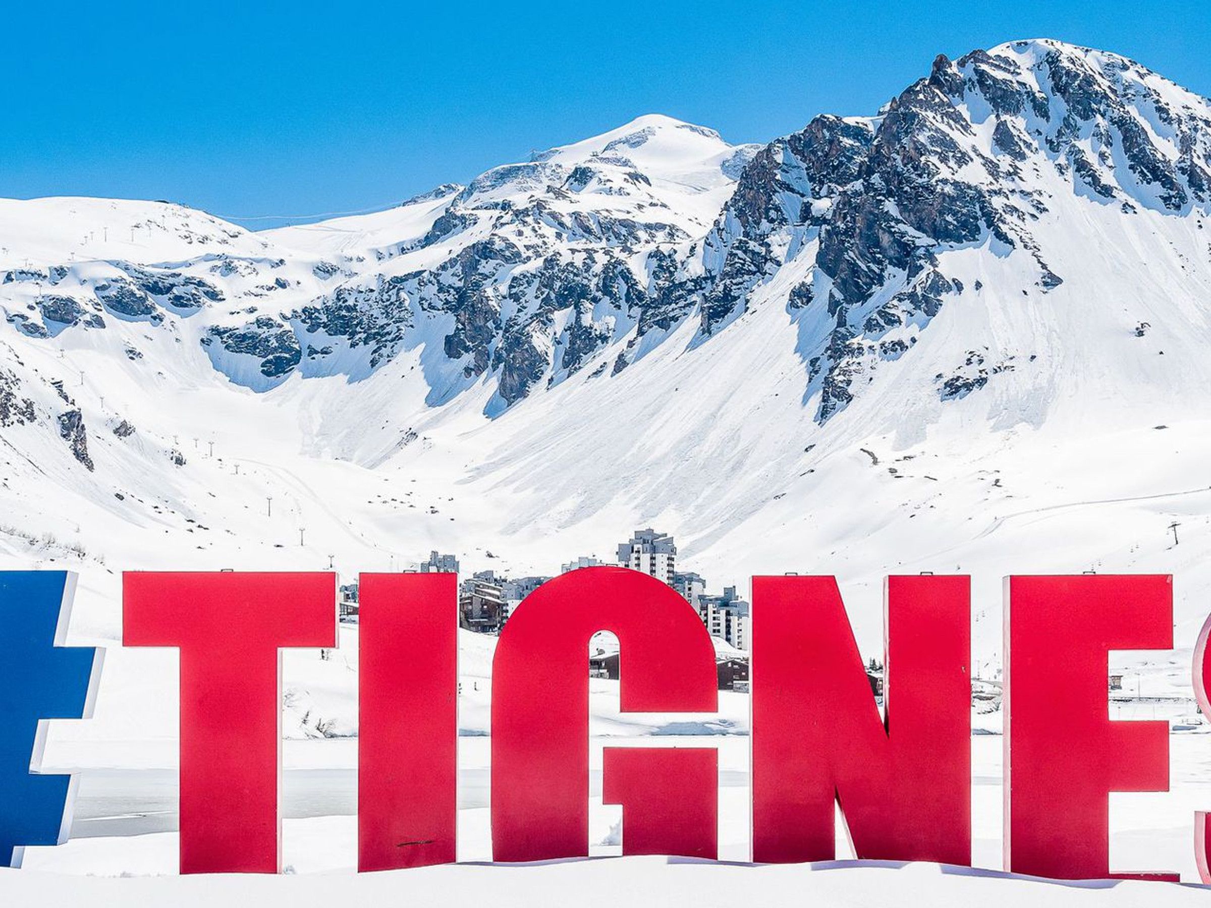 A snowy mountain landscape with large red letters spelling 'TIGNE' in the foreground.