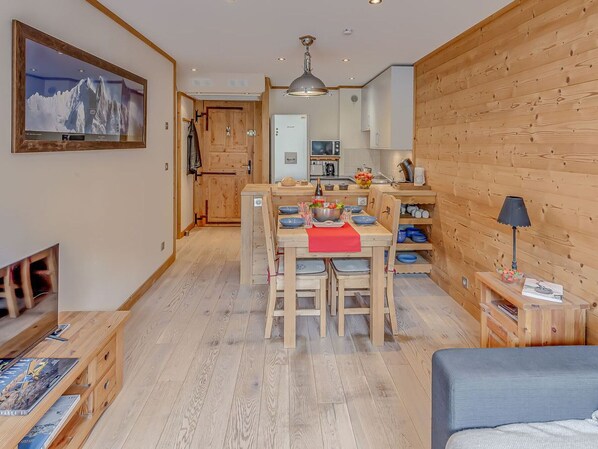 Un espacio habitable acogedor y moderno, con detalles de madera, un comedor con mantel individual rojo y una cocina con armarios de madera.