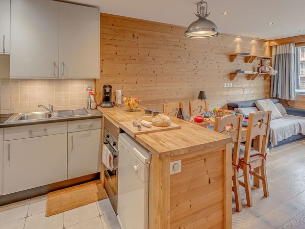 A modern kitchen with a wooden island, white cabinetry, and a dining area with a sofa and chairs. - Tignes - 3-room apartment, 6 pers, hotel services (Tignes)