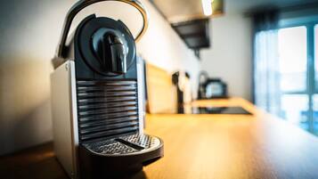 A coffee machine on a wooden table in a room with a window and a shelf in the background.
