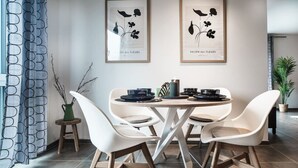 Un coin repas avec une table ronde, des chaises blanches et des reproductions botaniques encadrées accrochées au mur.